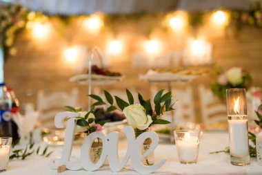 Şenlikli aşk gösterisi. Güzel düzenlenmiş bir masa, mumlarla, çiçeklerle ve lezzetli tatlılarla çevrili bir aşk işareti içerir..