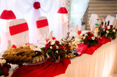 Etkinlikler için şık masa kurulumu. Parlak dekore edilmiş masa çeşitli yiyeceklere, zarif çiçeklere ve bir kutlama için güzel kırmızı aksanlara sahiptir..