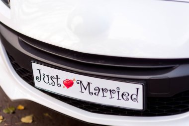 Bir düğün arabasında evlilik tabelası var. Beyaz bir araba neşeli bir evlilik tabelası sergiliyor. Düğün töreninden sonra gün ışığında evlilik tabelasını kutluyor..