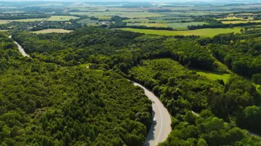 Yeşil Avrupa 'da virajlı yol. Avrupa 'da açık bir gökyüzü altında yoğun yeşil orman ve tarlalarla çevrili virajlı bir yolda araçlar seyahat eder..