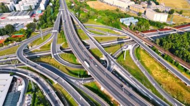 Avrupa 'da yoğun bir otoyol kavşağı var. Avrupa 'da gündüz vakti, araçlar yeşillik ve yakınlardaki binalarla karmaşık bir otoyol kavşağında yol alırlar..