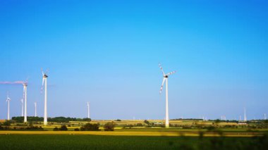 Türbinler temiz enerji üretir. Rüzgâr türbinleri berrak mavi gökyüzüne karşı dimdik durur ve sakin bir kırsal alanda yenilenebilir enerji üretirler..
