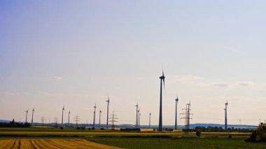 Güneşli kırsal rüzgar türbinleri. Rüzgâr türbinleri, parlak bir gökyüzünün altındaki geniş bir arazide, kırsal alanda yenilenebilir enerji sergilerler..