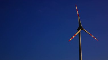 Açık mavi gökyüzüne karşı rüzgar türbini. Büyük bir rüzgar türbini açık mavi bir gökyüzünün altında gün boyunca keskin bıçaklarını sergiliyor..