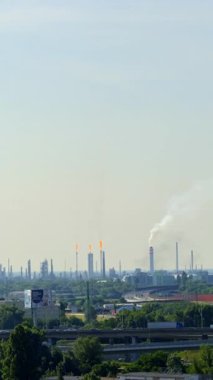 Duman bacaları ufuk çizgisinde. Yüksek baca ve işaret fişekleri ile geniş bir sanayi bölgesi açık bir gökyüzü altında etkin imalatı vurguluyor.