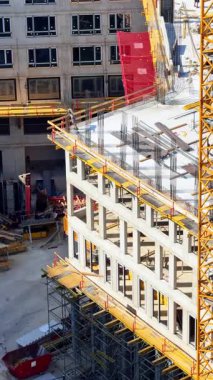 Ticari binalar gelişiyor. İşçiler ve makineler inşaat sahasında meşguller. İnşaat iskelesi ve beton yapılar gün ışığında görülebiliyor..