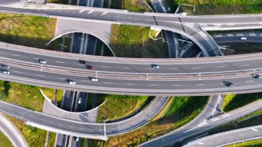 Karmaşık yol kavşağında yükselen araçlar hareket ediyor. Otoyollar, döngüler ve otoyollar üstten görünüyor.