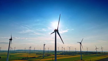 Dönen bıçaklı rüzgar değirmenlerinin siluetleri. Geniş tarlalardaki rüzgar türbinlerine düşük açılı görüş.