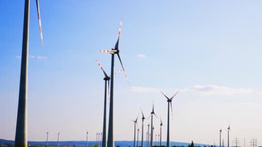 Yel değirmenlerinin kılıçları rüzgarda yavaşça döner. Mavi gökyüzünün arka planındaki rüzgar türbinlerine alçak açı görünümü.