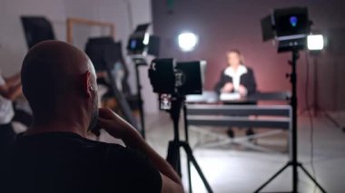 Kel sakallı kameraman sahne arkasında fotoğraf stüdyosunda çalışıyor. Modern profesyonel ekipmanlar bulanık arka planda oturan bir kadının videosunu kaydediyor..