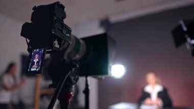 Tripodun üzerindeki kamera arka planda oturan bir bayanı çekiyor. Kapatın. Düşük açı. Stüdyoda video içeriği oluşturma.