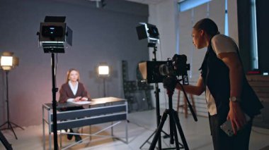 Kadın fotoğrafçı, kamerayı masada oturan kadına doğrultuyor. Stüdyoda günlük görüntüleri.
