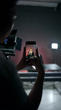 Tanımlanamayan bir kız elinde telefonla bir bayanı filme çekiyor. Stüdyoda video içeriği oluşturuluyor. Dikey video.