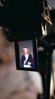 Beyaz kadın kamerada konuşur ve jestler yapar. Modern stüdyoda video çeken bir kamerayı kapat. Dikey video.