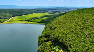 Sakin gölün yanında yemyeşil. Yeşil tepeler mavi gökyüzünün altında sakin bir göl üzerinde kule, güzel bir sahnede uzak dağlar tarafından çerçevelenmiş..
