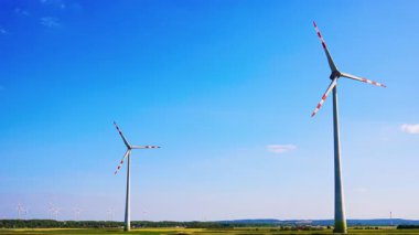 Rüzgâr türbinleri açık gökyüzünde dönüyor. Rüzgar türbinleri açık bir arazide, parlak mavi bir gökyüzü altında sürdürülebilir teknoloji gösteren yenilenebilir enerji üretir..