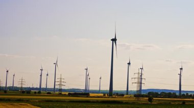 Rüzgar türbinleri temiz enerji üretir. Uzun rüzgar türbinleri açık mavi gökyüzünün altında, sürdürülebilir enerjiyi ön plana çıkaran kırsal bir alanda dönerler..
