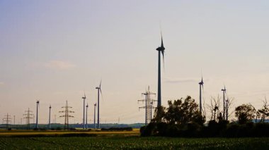 Türbinler temiz enerji üretir. Büyük rüzgar türbinleri kırsal bir alanda uzun süre ayakta kalarak günbatımında sürdürülebilir enerji üretimini sergiliyor..