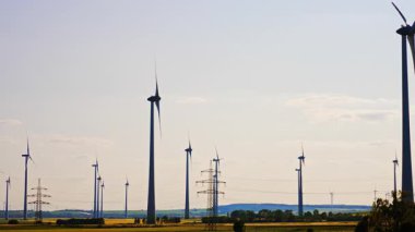 Geniş alanda akıl türbinlerinin siluetleri. Elektrik destekleri yakınlarda. Enerji kavramı.