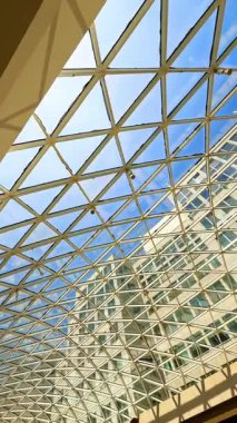 Modern tasarımda geometrik tavan. Modern bir binanın geometrik cam tavanından parlak mavi gökyüzü, kentsel tasarımı vurguluyor..