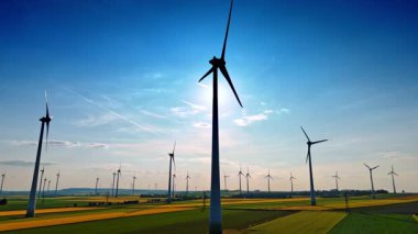 Parlak bir manzarada türbinler. Rüzgâr türbinleri güneşli bir günde ufuk çizgisinde sakin bir kırsal alanda yenilenebilir enerji üretirler..