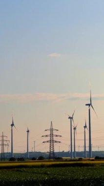 Rüzgardan yenilenebilir enerji. Rüzgar türbinleri açık bir gökyüzüne karşı dimdik dururlar. Gün batımında yeşil bir tarlada rüzgar enerjisini kullanırlar..