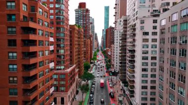 Yoğun cadde boyunca uzanan çok katlı güzel binaların cephelerinde uçmak. Uzun düz yolda birden fazla araba hareket ediyor. New York, ABD.