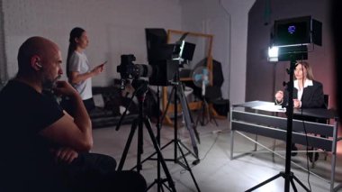 Odaklanmış erkek fotoğrafçı kameraya bakar esmer, beyaz kadına bakar. Beyaz tişörtlü kadın elinde telefonla arka planda duruyor. Bir blogun stüdyo görüntüleri.