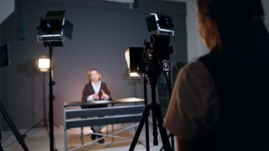 Tanımlanamayan kadın sahne arkasında kameranın arkasında duruyor. Kadın bulanık arka planda masasında oturuyor konuşuyor ve el sallıyor..