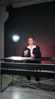 Siyah ceketli esmer kadın stüdyoda kameraya konuşuyor. Blog çekimlerinin kulisinde. Dikey video.