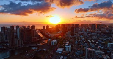 Göz kamaştırıcı batan güneş gökyüzünü ve ufuktaki bulutları aydınlatıyor. İnsansız hava aracı günbatımında Honolulu, Hawaii, ABD manzarasının üzerinde..