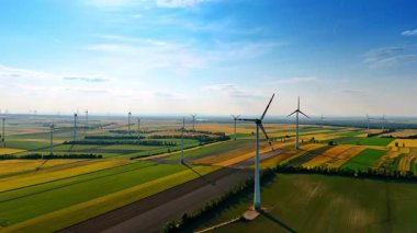 Yeşil alanlarda rüzgar türbinleri. Rüzgar türbinleri, yenilenebilir enerji çabalarını ön plana çıkaran açık mavi gökyüzünün altındaki geniş yeşil alanlar boyunca zarifçe dönerler..