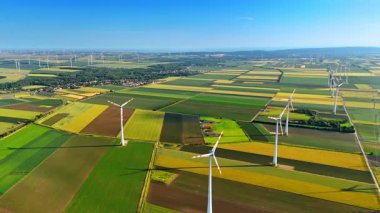 Rüzgar türbinleri temiz alanlarda. Rüzgar türbinleri, parlak yeşil ve sarı alanlarda, güneşli bir arazide yenilenebilir enerji sergilerler..