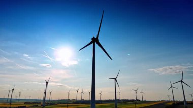 Türbinler kırsal alanda yeşil enerji üretir. Rüzgâr türbinleri, güneşli bir günde, açık mavi gökyüzüne karşı dimdik ayakta duruyor..