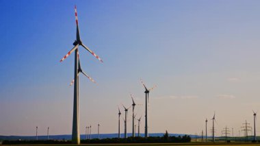 Gün ışığı rüzgar türbini enerjisi. Uzun rüzgar türbinleri açık gökyüzünde dönüyor, kırsal alanda güneşli bir günde yenilenebilir enerjiyi kullanıyorlar..