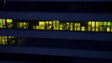 Footage at the facade of the office building at dark time of the day. Drone flight along the floors with light switched on in the rooms.