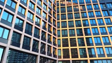 Çok katlı bir binanın modern cephesi. Komşu bina pencerelere yansıyor. Düşük açı görünümü.