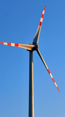 Rüzgar türbini açık gökyüzünün altında dönüyor. Büyük bir rüzgar türbini, güneşli bir günde yenilenebilir enerjiyi kullanan açık mavi bir gökyüzü üzerinde döner..