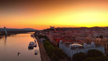 Bratislava, Slovakya 'nın muhteşem günbatımı manzarasını renklendiriyor. İnsansız hava aracı şehrin tarihi kısmından yükseliyor. Şehir manzarası ve Tuna Nehri üzerinde turuncu gökyüzü.