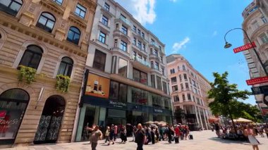 Viyana, Avusturya - 9 Haziran 2025: Eski tarihi binalarda büyük vitrinleri olan modern dükkanlar. Avusturya 'nın Viyana kentindeki güzel yaya caddesinin yanından geçen turistler ve yerliler.