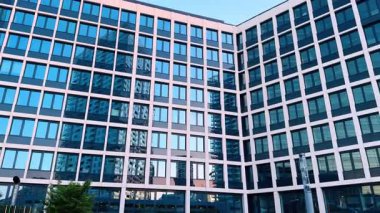 Bratislava, Slovakya - 5 Haziran 2025: Cam pencereli şehir binası. Çağdaş bir binanın yansıtıcı pencereleri açık mavi gökyüzü altında kentsel bir ortamda yakın yapıları yakalar.