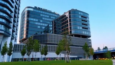 Bratislava, Slovakya - 5 Haziran 2025: Kentsel ortamdaki modern ofis binası. Dışı cam kaplamalı gösterişli bir ofis yapısı yeşil bir alanda duruyor. Günbatımında çağdaş mimari sergileniyor..