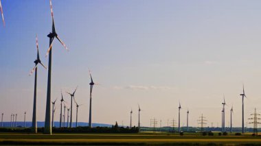 Kırsal alanda rüzgar türbinleri. Rüzgâr türbinleri kırsal bir ortamda gün boyunca açık mavi gökyüzünün altında rüzgar enerjisini kullanarak dimdik dururlar..