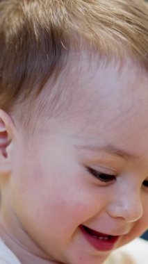 Mutlu bir yıllık bebek portresi. Gülümseyen beyaz çocuk yaklaş. Arkaplan bulanık. Dikey video