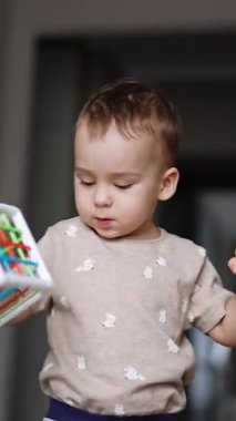 Odanın önünden geçerken oyuncak küpünü sallayan güzel çocuk. Bebek evde bir oyuncakla oynuyor. Kapatın. Dikey video