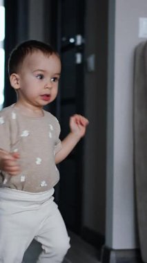 Küçük erkek bebek odaya koştu. Çocuk kamerayı fark eder ve elini uzatır. Dikey video