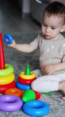 Akıllı küçük çocuk oyuncaklarıyla yerde oynuyor. Piramitleri birleştiren güzel bebek. Yüksek açı. Dikey video