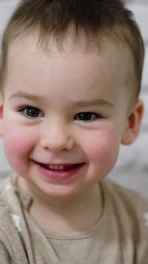 Kameraya sevimli bir şekilde gülümseyen beyaz bir çocuk. Yeni yürümeye başlayan bir çocuğun yakın portresi. Dikey video