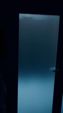 Hastanedeki kapının yanında yürüyen koyu renk erkek silueti. Koca, karısının doğum yapmasından dolayı gergin. Dikey video