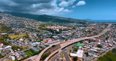 Karayolu boyunca ilerleyen bir araç engin alçak şehir manzarasını geçiyor. Dağlarda asılı dramatik bulutlar. Honolulu, Hawaii, ABD. Hava perspektifi.